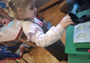 dzieci ubrane w brązowe fartuszki biorą udział w czekoladowych warsztatach, samodzielnie ozdabiają czekoladę w kształcie serca