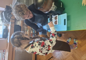 dzieci ubrane w brązowe fartuszki biorą udział w czekoladowych warsztatach, samodzielnie ozdabiają czekoladę w kształcie serca