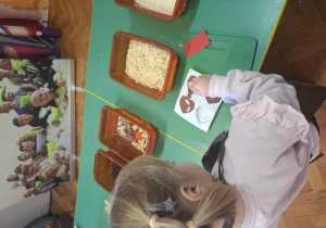 dzieci ubrane w brązowe fartuszki biorą udział w czekoladowych warsztatach, samodzielnie ozdabiają czekoladę w kształcie serca