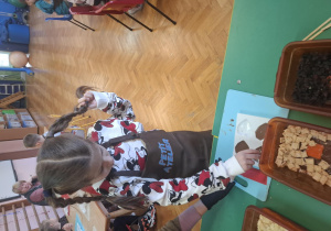 dzieci ubrane w brązowe fartuszki biorą udział w czekoladowych warsztatach, samodzielnie ozdabiają czekoladę w kształcie serca