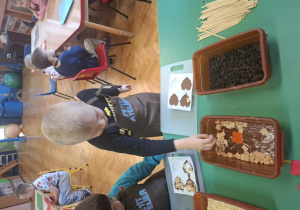 dzieci ubrane w brązowe fartuszki biorą udział w czekoladowych warsztatach, samodzielnie ozdabiają czekoladę w kształcie serca