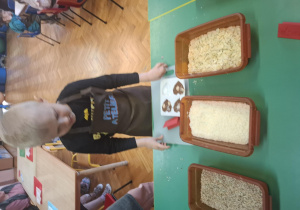 dzieci ubrane w brązowe fartuszki biorą udział w czekoladowych warsztatach, samodzielnie ozdabiają czekoladę w kształcie serca