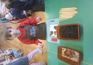 dzieci ubrane w brązowe fartuszki biorą udział w czekoladowych warsztatach, samodzielnie ozdabiają czekoladę w kształcie serca