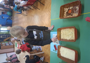 dzieci ubrane w brązowe fartuszki biorą udział w czekoladowych warsztatach, samodzielnie ozdabiają czekoladę w kształcie serca