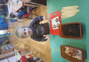 dzieci ubrane w brązowe fartuszki biorą udział w czekoladowych warsztatach, samodzielnie ozdabiają czekoladę w kształcie serca