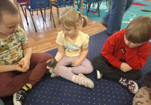 dzieci siedzą w kole na dywanie, podają sobie małego żółwia