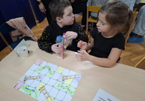 chłopiec i dziewczynka siedzą przy stoliku i grają w grę planszową