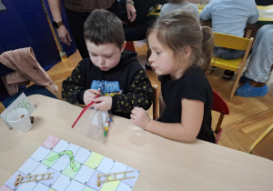 chłopiec i dziewczynka siedzą przy stoliku i grają w grę planszową