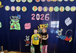 cgłopiec i dziewczynka pozują do zdjęcia na tle napisu Mini Olimpiada Gier Planszowych