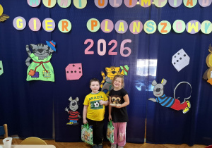 cgłopiec i dziewczynka pozują do zdjęcia na tle napisu Mini Olimpiada Gier Planszowych