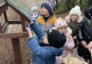 Dzieci dokarmiają ptaki w ogrodzie przedszkolnym.