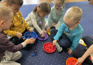 Na dywanie dzieci przeliczają figurki.