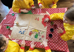 Dzieci przy stolikach malują rekami na dużych formatach.