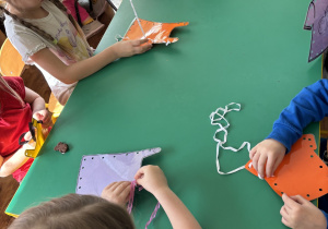 Dzieci siedzą przy stolikach i szyją ubrania.