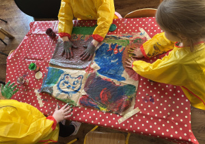 Dzieci przy stolikach malują rekami na dużych formatach.