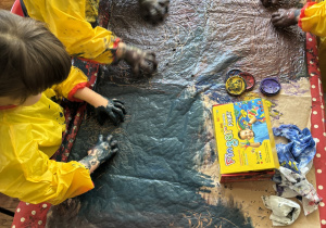 Dzieci przy stolikach malują rekami na dużych formatach.