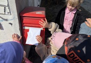 Dzieci wrzucają do skrzynki pocztowej list dla koleżanki.