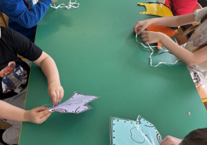 Dzieci siedzą przy stolikach i szyją ubrania.