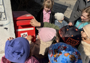 Dzieci wrzucają do skrzynki pocztowej list dla koleżanki.