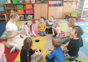 dzieci razem z panią siedzą w kole i przyglądają się królikom