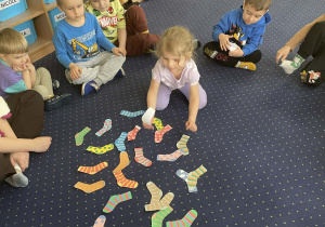 Dzieci siedzą w kole na dywanie i kompletują skarpetki.