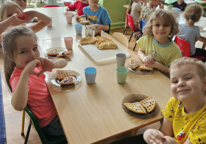 Dzieci siedzą przy stole i jedzą gofry.