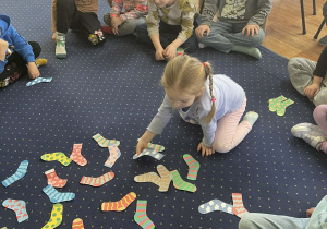 Dzieci siedzą w kole na dywanie i kompletują skarpetki.