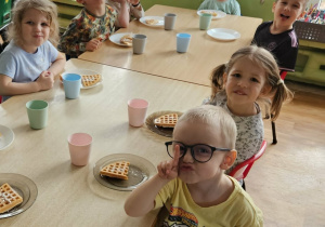 Dzieci siedzą przy stole i jedzą gofry.