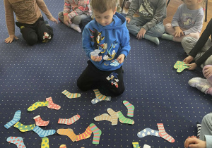 Dzieci siedzą w kole na dywanie i kompletują skarpetki.