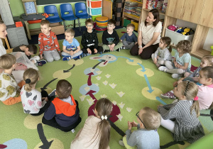 Dzieci siedzą w kole i słuchają pani.