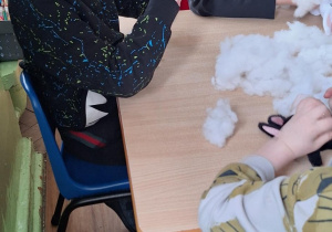 Dzieci siedzą przy stole i wypełniają zajączki kulką silikonową.
