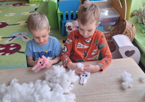 Dzieci siedzą przy stole i wypełniają zajączki kulką silikonową.