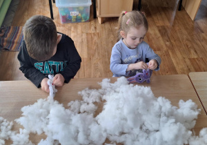 Dzieci siedzą przy stole i wypełniają zajączki kulką silikonową.