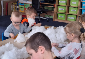 Dzieci siedzą przy stole i wypełniają zajączki kulką silikonową.