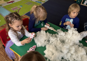 Dzieci siedzą przy stole i wypełniają zajączki kulką silikonową.