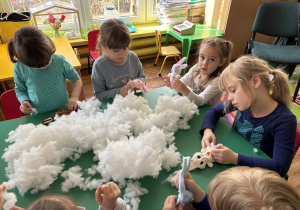 Dzieci siedzą przy stole i wypełniają zajączki kulką silikonową.