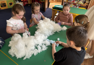 Dzieci siedzą przy stole i wypełniają zajączki kulką silikonową.