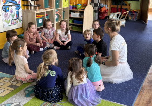 Dzieci siedzą w kole i słuchają pani.
