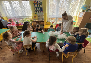 Dzieci siedzą przy stole i wypełniają zajączki kulką silikonową.