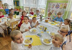 Dzieci siedzą przy stołach i zjadają obiad.