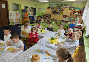 Dzieci siedzą przy stołach i zjadają obiad.