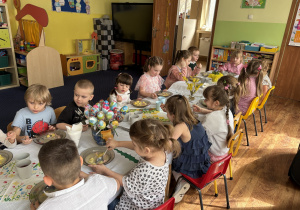 Dzieci siedzą przy stołach i zjadają wielkanocny obiad.