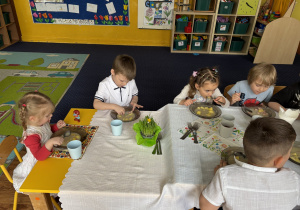 Dzieci siedzą przy stołach i zjadają wielkanocny obiad.