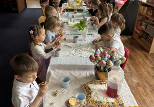 Dzieci siedzą przy stołach i zjadają słodkości.