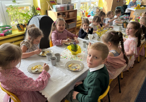 Dzieci siedzą przy stołach i zjadają wielkanocny obiad.