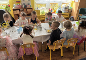 Dzieci siedzą przy stołach i zjadają wielkanocny obiad.