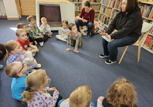 Dzieci siedzą na dywanie i słuchają pani.