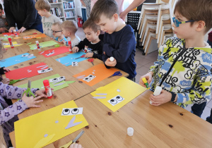 Dzieci przy stołach wykonują prace plastyczne.