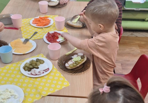 Dzieci siedzą przy stole i zjadają samodzielnie przygotowane śniadanie.