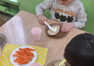 Dzieci siedzą przy stole i zjadają samodzielnie przygotowane śniadanie.